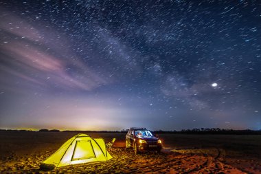 Nikolaevka, Rusya - 04 Mayıs 2019: Nehirde gece kampı. Gökyüzündeki yıldız izleri. Çadırın yanında siyah bir geçit duruyor.