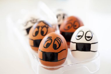 Farklı boyalı yüzleri ve tıbbi maskeleri olan yumurtalar.