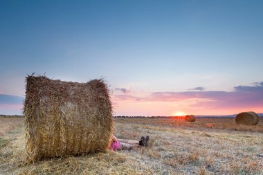 Adam bir balya saman üzerinde günbatımında dinlenme