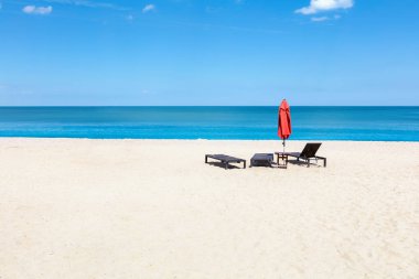 Sahilde üç şezlong ile kırmızı umbrealla