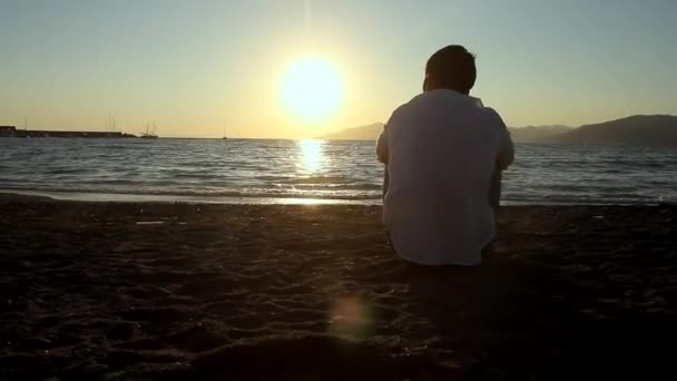 Mężczyzna siedzi na plaży — Wideo stockowe
