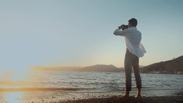 Muž na pláži s dalekohledem — Stock video