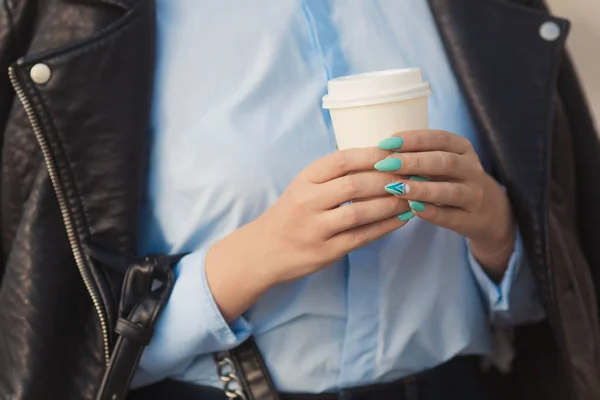 Mujer elegante con manicura colorida en chaqueta de cuero sosteniendo en las manos una taza de papel de café Fotos de stock