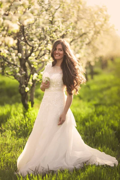 Retrato de mujer hermosa en flores. La novia en vestido de novia de marfil con pelo largo y rizado caminando en jardines con árboles de flores de verano —  Fotos de Stock