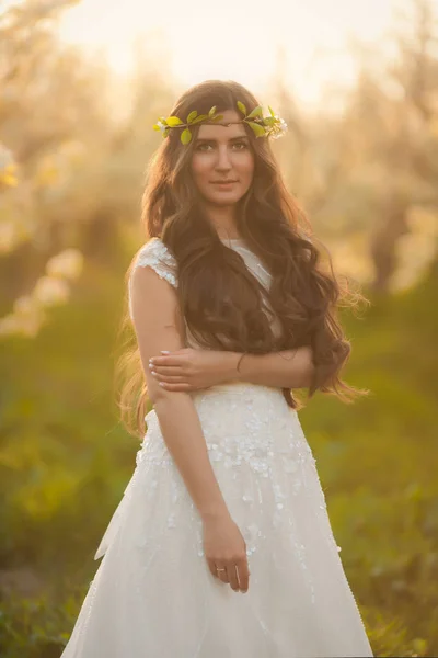 Retrato de mujer hermosa en flores. La novia en vestido de novia de marfil con pelo largo y rizado caminando en jardines con árboles de flores de verano —  Fotos de Stock