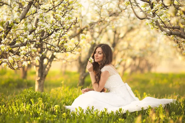 Çıtır güzel kadın portresi. Fildişi gelinlikle bahçelerde yaz çiçeği ağaçları ile yürüyüş uzun kıvırcık saçlı gelin — Stok fotoğraf