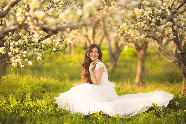 Portret van mooie vrouw in bloemen. De bruid in ivoor trouwjurk met lang krullend haar wandelen in tuinen met zomer bloesem bomen — Stockfoto