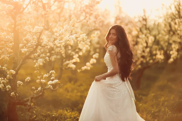 Retrato de mujer hermosa en flores. La novia en vestido de novia de marfil con pelo largo y rizado caminando en jardines con árboles de flores de verano —  Fotos de Stock