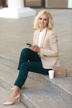 Gülümseyen, cep telefonu açık havada tutan ve kameraya bakıyor güzel iş kadını moda giysiler