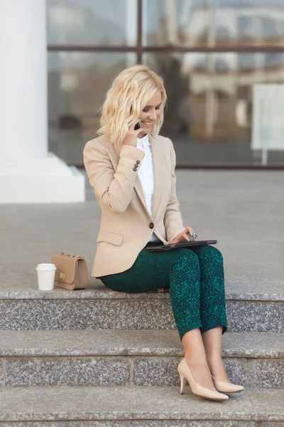 Hermosa mujer de negocios en ropa de moda sonriendo, sosteniendo el teléfono móvil al aire libre y mirando a la cámara — Foto de Stock