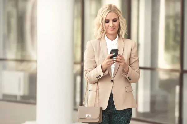 Gülümseyen, cep telefonu açık havada tutan ve kameraya bakıyor güzel iş kadını moda giysiler