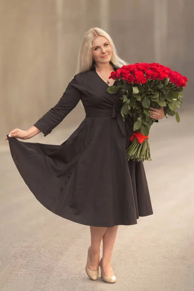 在黑色复古礼服美丽的金发女人的肖像持有100红玫瑰户外大花束 惊喜礼物日期 — 图库照片