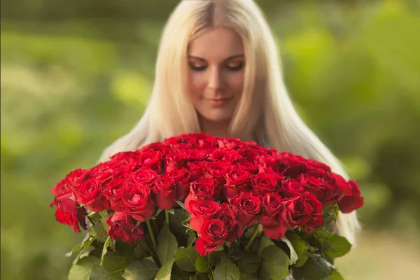 在黑色复古礼服美丽的金发女人的肖像持有100红玫瑰户外大花束 惊喜礼物日期 — 图库照片