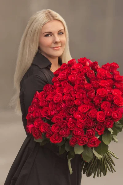 Portrait of beautiful blonde woman in black retro dress holding big bouquet of one hundred red roses outdoor. Surprise gift on date. — Stock Image Portrait Beautiful Blonde Woman Black Retro Dress Holding Big Bouquet Stock Image