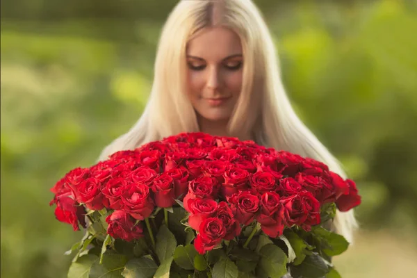 Portrait of beautiful blonde woman in black retro dress holding big bouquet of one hundred red roses outdoor. Surprise gift on date. — Stock Image Portrait Beautiful Blonde Woman Black Retro Dress Holding Big Bouquet Stock Picture