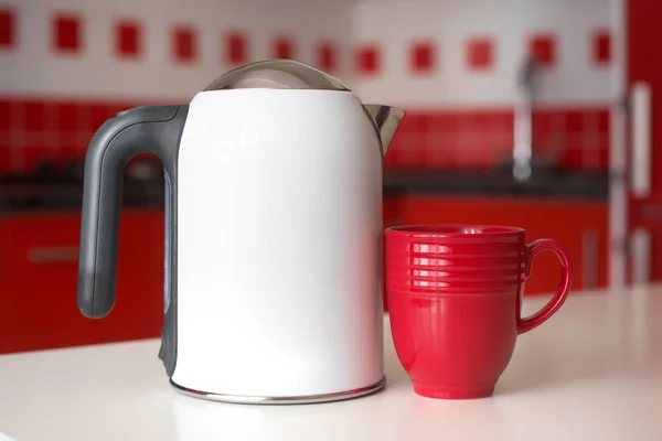 Electric kettle with cup on a table of red and white kitchen interior