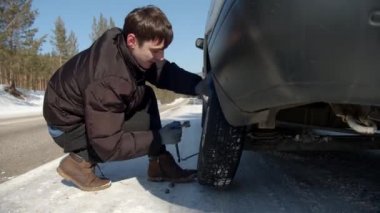 Sibirya 'da güneşli bir kış gününde araba tekerleği değiştiren bir adam.