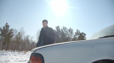 Güneşli kış gününde kaputun altında araba tamir eden bir adam.