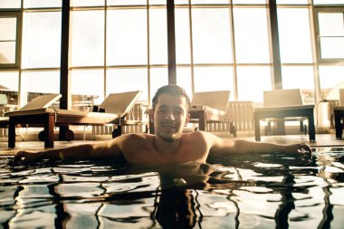 Esmer adam, kapalı bir yüzme havuzunun kenarında dinleniyor.