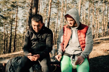 Asyalı ve Kafkasyalı iki arkadaş Çam Ormanı 'nda akıllı telefondan bir şey izliyorlar.