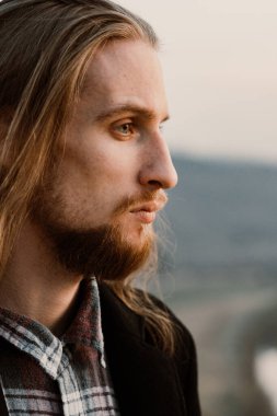 Gün batımında tepedeki uzun saçlı, sakallı yakışıklı adamın portresi.