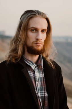 Gün batımında tepedeki uzun saçlı, sakallı yakışıklı adamın portresi.