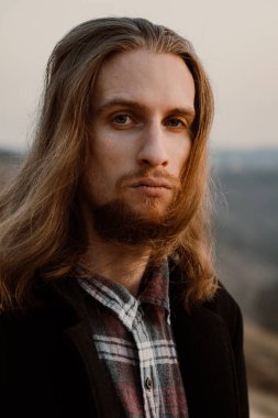 Gün batımında tepedeki uzun saçlı, sakallı yakışıklı adamın portresi.