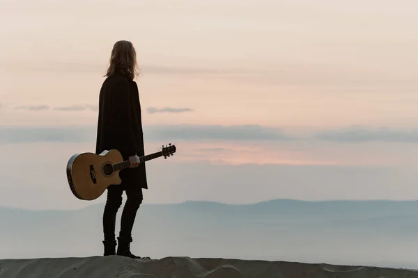 Sibirya 'da gün batımında kum tepesinde gitarlı uzun saçlı sakallı bir adam duruyordu.
