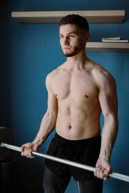 Yakışıklı adam odanın ortasında halterle egzersiz yapıyor.