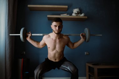 Yakışıklı adam odanın ortasında halterle egzersiz yapıyor.