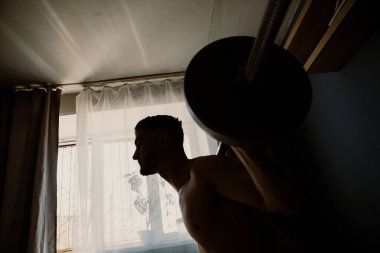 Yakışıklı adam odanın ortasında halterle egzersiz yapıyor.