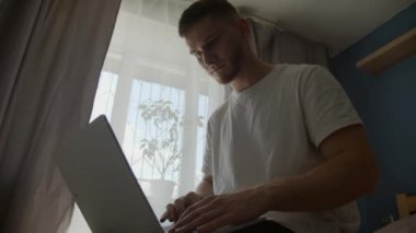 Adam dizüstü bilgisayar kullanıyor, yatakta oturuyor. 