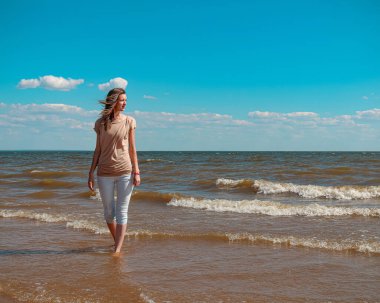 Suyun kenarında sahilde yürüyen güzel genç bir kadın.
