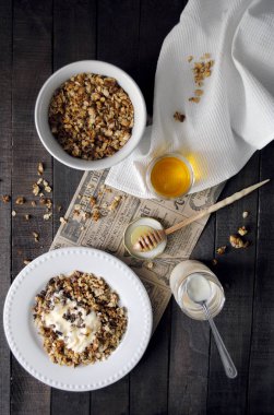Ev yapımı yulaf ezmesi granola fıstık, yoğurt ve bal karanlık masada beyaz plakaları ile güneşli sabah