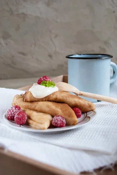 Indah pancake Rusia dengan krim asam, raspberry dan cangkir antik teh di latar belakang beton — Stok Foto