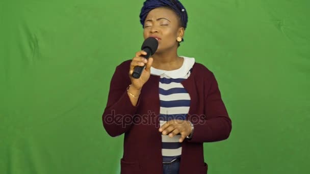 Красива молода жінка співає. Молода співачка співає в мікрофон на зеленому фоні . — стокове відео