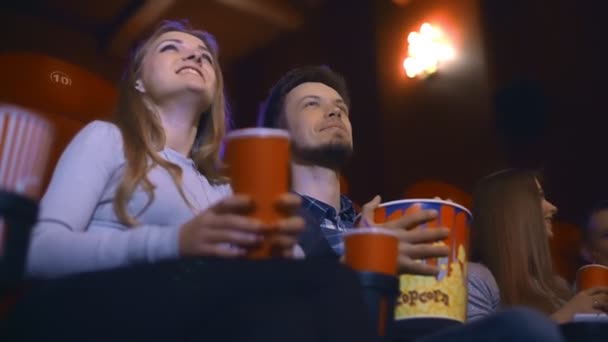 Szczęśliwa para siedzi w kinie, oglądając film, jedzenie popcorn, picia i uśmiechając się. — Wideo stockowe