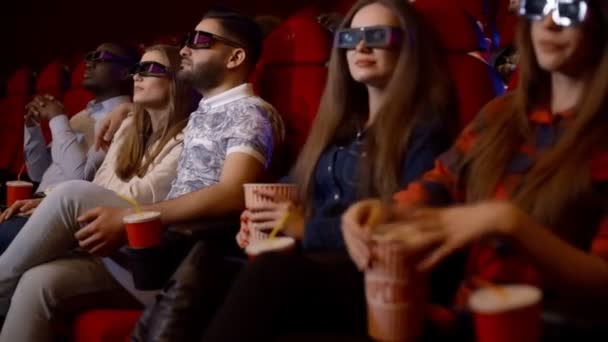 Amigos do cinema assistindo a um filme fascinante em óculos 3D, bebendo cola e comendo pipocas . — Vídeo de Stock