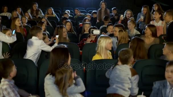 Девочки и мальчики в кино смотрят на девочку в очках виртуальной реальности . — стоковое видео