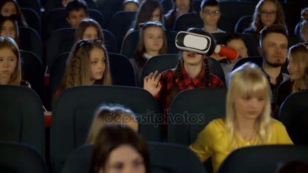 Девочки и мальчики в кино смотрят на девочку в очках виртуальной реальности . — стоковое видео