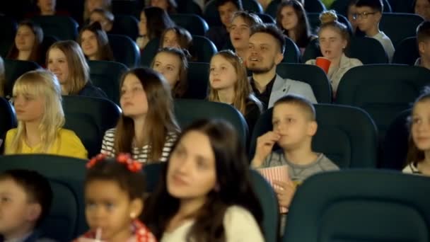 Crianças entusiasticamente olhando desenhos animados alegres no salão de cinema . — Vídeo de Stock