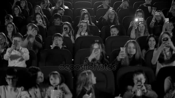 Šťastné děti v kině hledá karikatury a telefon bliká. Černá a bílá zastřelil. — Stock video