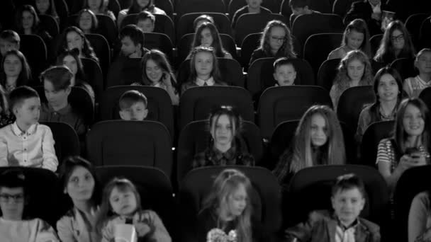 Happy children in the cinema looking a cartoon and make phone flashes. Black and white footage. — Stock Video