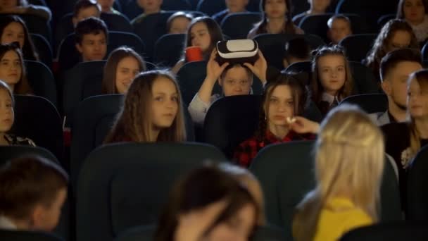 Niñas y niños en el cine viendo a un niño con gafas de realidad virtual . — Vídeo de stock