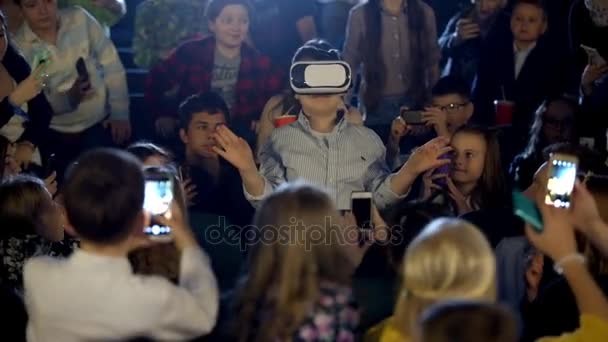 Niñas y niños en el cine viendo a un niño con gafas de realidad virtual . — Vídeo de stock