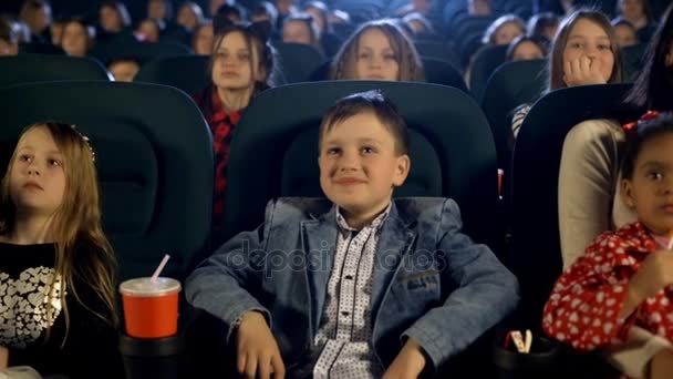 Маленькі дівчата і хлопчики дивляться фільм і їдять попкорн у кінотеатрі — стокове відео