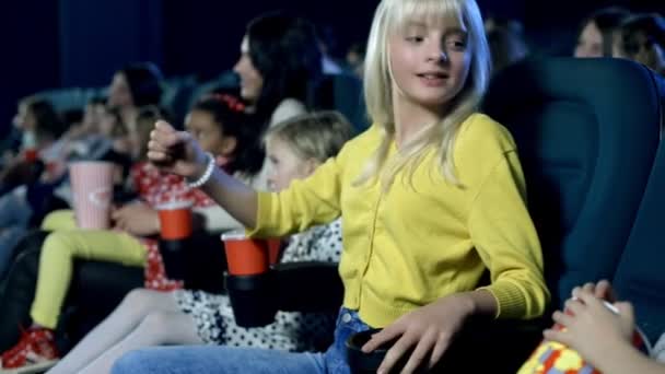 Menina bonito com seus amigos emocionalmente assistindo filme no cinema . — Vídeo de Stock