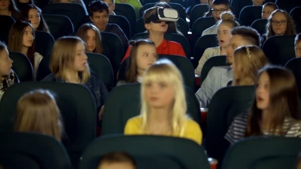 Little children teens at the cinema watching at boy in virtual reality glasses. — Stock Video