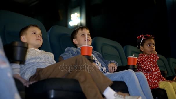 Glimlachend weinig jongens en meisje kijken film in de bioscoop, en drinken cola, close-up. — Stockvideo