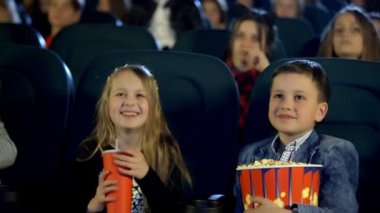 Küçük çocuk ve arkadaşları patlamış mısır yemek ve coşku ile sinemada film izleme,